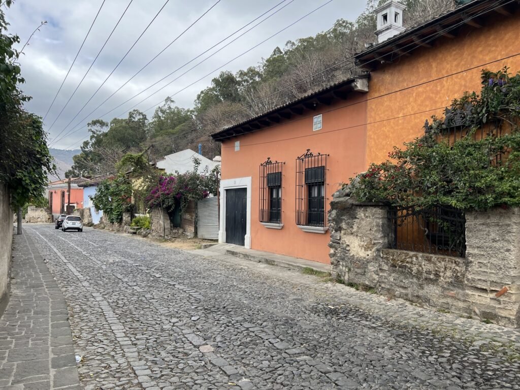 A quiet cobblestone street in Antigua, Guatemala, lined with terracotta and orange colonial houses